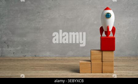 Toy rocket positioned on a staircase of wooden blocks showing the stages of a successful startup launch. Stock Photo