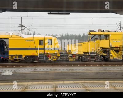 Krakow, Poland - December 3, 2025: Two yellow Plasser & Theurer railway maintenance machines are parked side by side on train tracks, signifying railw Stock Photo