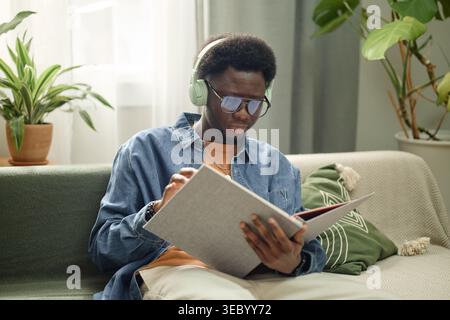 Black Man Wearing Headphones Reading Book for Online Learning Stock Photo