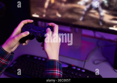Person Playing Video Game With Controller in Front of Computer Screen in Low Light Stock Photo