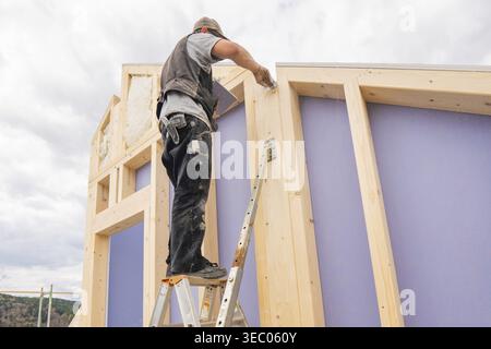 Man standing on ladder and working on timber frame construction under cloudy sky, residential building renovation, Nagold, Calw district, Germany Stock Photo