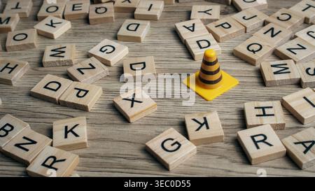 Caution cone surrounded by scattered wooden letter tiles on a wooden background representing word search and warning concepts. Stock Photo