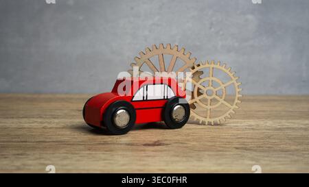 Red toy car with wooden gears in the background representing automotive engineering and mechanics. Stock Photo