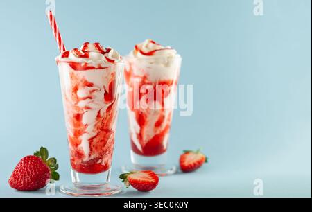 Strawberry milkshake with whipped cream and berry syrup in the tall glass on blue background. Stock Photo