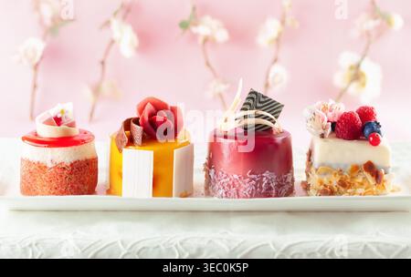 Various mini cakes on a white plate. Sweets decorated with fresh berries and flowers for holiday. Stock Photo