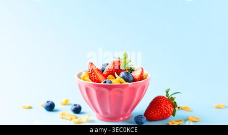 Concept of healthy gluten free breakfast with berries,natural yogurt and corn flakes in the pink bowl on blue background. Stock Photo