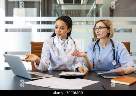 Two diverse medical professionals, a doctor and a nurse, discussing test results displayed on a laptop, sharing expertise and working together in a mo Stock Photo