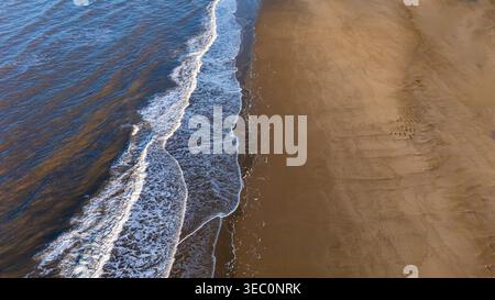 Aerial top down drone view of the tide and waves on the sandy beach Stock Photo
