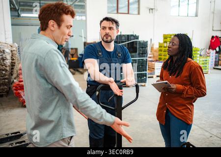 Diverse group of logistics workers having a serious conversation in a warehouse Stock Photo