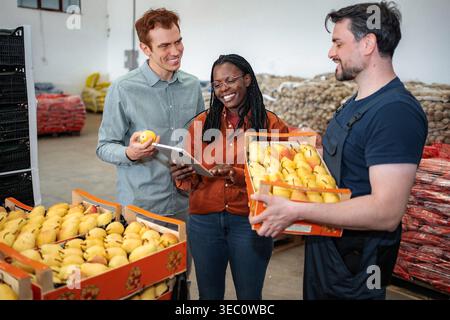 Diverse team examining fresh produce and using digital tablet for inventory management Stock Photo