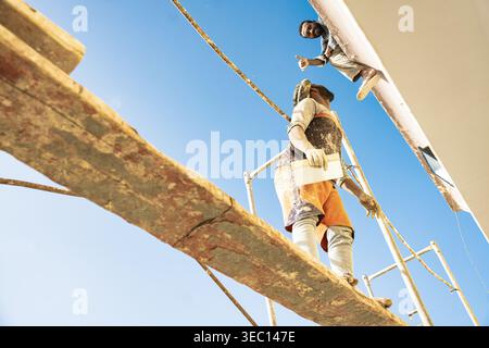 Marsa alam, egypt 21 april 2026: construction workers collaborating on scaffolding under a clear blue sky, showing manual labor and teamwork on a buil Stock Photo