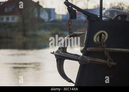 An anchor hanging on a chain on the bow of a small river icebreaker. The black side of the ship with an anchor. River icebreaker. Stock Photo