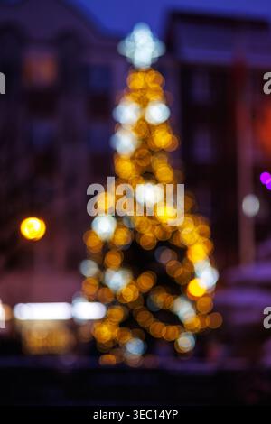 A defocused image of a Christmas tree with garlands. Bright yellow and white lights on the tree are in the bokeh area. A festive mood. Stock Photo