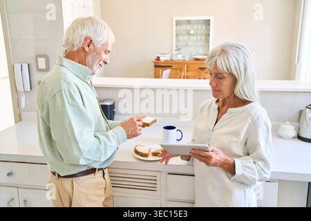 Healthy aging and digital inclusion — a senior couple enjoys a relaxed breakfast in their bright kitchen. Stock Photo