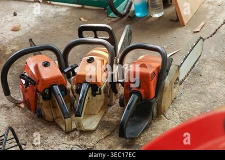 Powerful orange chainsaw power tool equipment resting on concrete floor of workshop. Heavy motor machine ready for cutting tough timber. Strong mechan Stock Photo