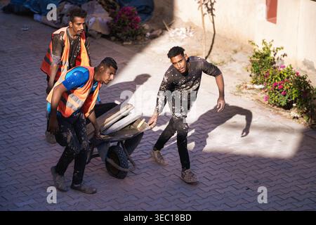Marsa alam, egypt 21 april 2026: construction workers hauling heavy stone slabs with a wheelbarrow on a sunlit paved street, teamwork and hard manual Stock Photo