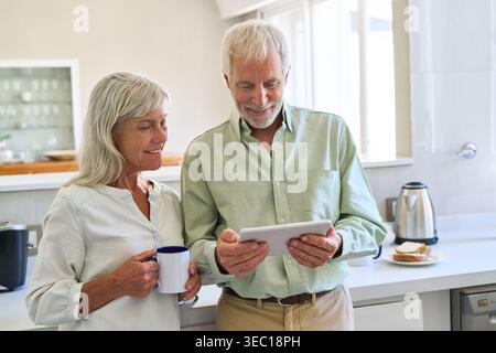 Senior digital inclusion and healthy aging, with a happy elderly couple using a digital tablet together in their modern kitchen. Stock Photo