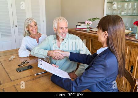 This depicts a senior couple engaged in retirement planning and financial protection, shaking hands with a professional advisor. Stock Photo