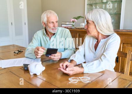 Retirement planning and financial security — a senior couple is seated at a wooden table at home, engaged in a serious discussion about their finances Stock Photo