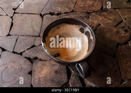 Looking down at an empty coffee cup with leftover milk foam inside. dark ceramic mug resting on rustic wooden table gives off relaxing, satisfying, an Stock Photo