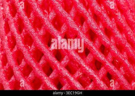 Bright red foam net packaging wrapper texture macro photography showing intricate mesh pattern over vibrant pink background creating abstract textured Stock Photo