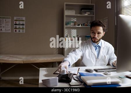 Adult Male Doctor Working at Desk in Clinic Office Stock Photo