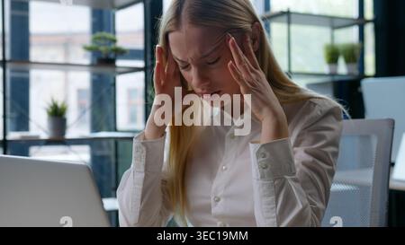 Tired ill sick fatigued Caucasian businesswoman holding head pain headache working laptop business woman irritated with computer problem error failure Stock Photo