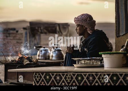 Marsa alam, egypt 21 april 2026: bedouin man in keffiyeh preparing traditional tea over a campfire in egypt’s marsa alam desert at sunrise, serene and Stock Photo