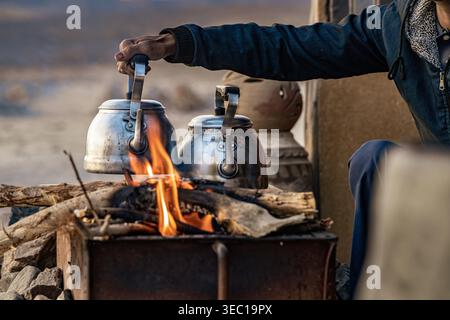 Marsa alam, egypt 21 april 2026: bedouin man brewing tea in metal kettles over an open campfire in the desert, offering traditional hospitality and wa Stock Photo