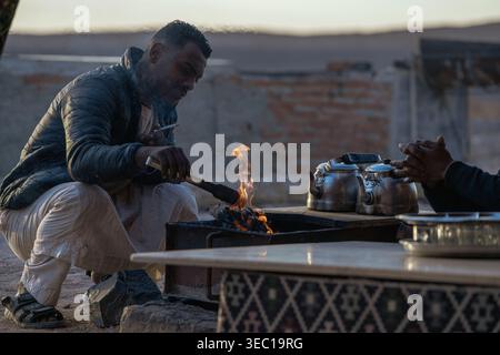 Marsa alam, egypt 21 april 2026: bedouin man preparing traditional tea on a campfire in the marsa alam desert, featuring kettles and a shared experien Stock Photo