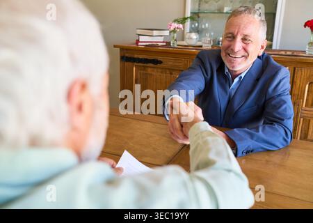 Retirement planning and financial protection — a senior client is shaking hands with a smiling financial advisor, signifying an agreement or successfu Stock Photo