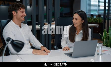 Two happy laughing Caucasian business woman and man working together with papers laugh humorous ridiculous smile colleagues with documents and laptop Stock Photo