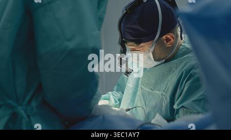 Two medics in operation room working together skilled doctor man surgeon physician medic work busy with operation operating patient with nurse intern Stock Photo