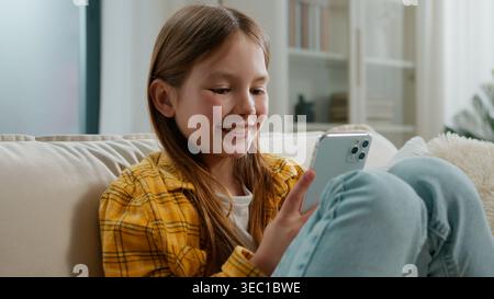 Happy Caucasian kid girl looking in mobile phone texting chatting message in social media networks smiling child daughter preteen user with smartphone Stock Photo
