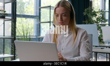 Serious Caucasian businesswoman typing laptop female operator in headset talking with client business woman browsing computer modern technology girl Stock Photo