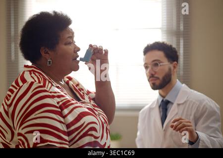 Black Middle Aged Woman Using Inhaler during Medical Consultation Stock Photo
