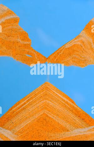 Moving sand art showing symmetrical golden pyramid forming under blue sky background with texture Stock Photo