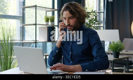 Indian ethnic Arabian businessman checking papers talking call looking in laptop ethnicity business man guy male worker employer agent talk mobile Stock Photo