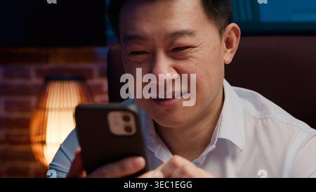 Closeup smiling Asian 40s business man look in mobile phone enjoying pleasant chatting online happy Korean businessman Chinese specialist Japanese Stock Photo