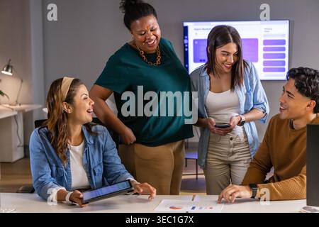 Diverse coworkers discussing project, reviewing charts, tablet and monitor at white table Stock Photo