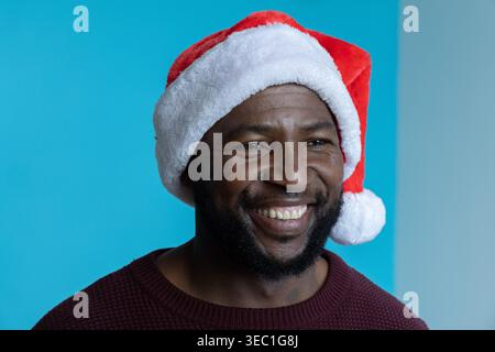 African American man smiling and wearing red Santa hat and maroon sweater in studio Stock Photo