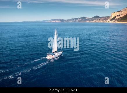 Aerial view of floating sailboat and rocky sea coast at sunny day Stock Photo
