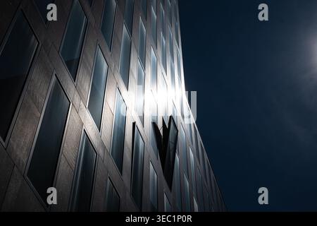 Detailed view of a contemporary corporate building exterior. Features a repeating grid of windows with a sun flare reflection and a single open window Stock Photo