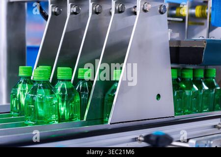 green plastic PET bottles moving on conveyor belt in drink beverage manufacturing factory. Automated production line machinery process for drinking wa Stock Photo