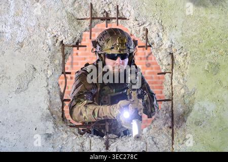 Tactical Soldier With Rifle Pointing Through Bullet-Hole Wall During Urban Combat Training Stock Photo