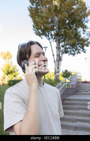 smiling man talking on phone in park . Everyday life. Communication via mobile phone. Young man 30 years old smiling, laughing, looking excited, surpr Stock Photo