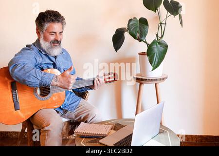 Person playing guitar, learning during a virtual music class with a laptop Stock Photo