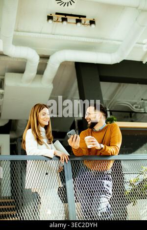 Two friends share a joyful moment at a stylish cafe, chatting and enjoying drinks while leaning over a railing in a trendy space. Stock Photo
