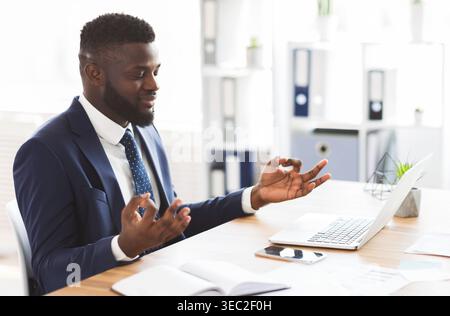 African american businessman meditating in office, relaxing during working Stock Photo