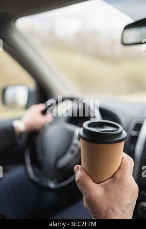 Close up of hand holding takeaway coffee cup inside car driving transport lifestyle concept commute beverage modern daily routine Stock Photo